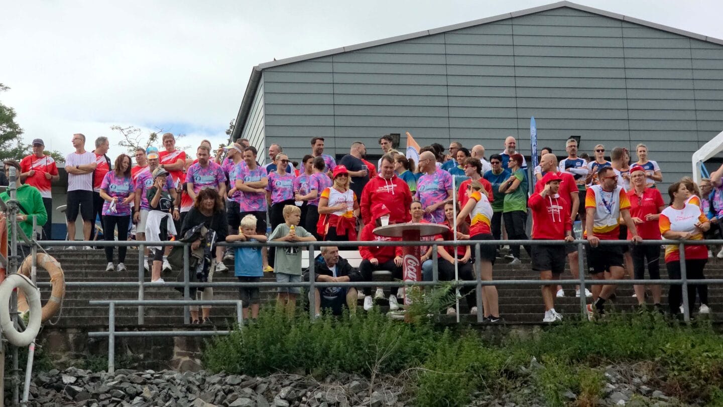 Eine große Gruppe von Menschen in verschiedenen bunten Trikot stehen auf einer großen Tribühne.