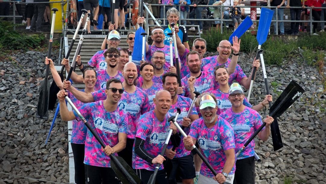 Eine Gruppe von Menschen sthene in bunten T-Shirts und Paddeln in der hand und jubeln.