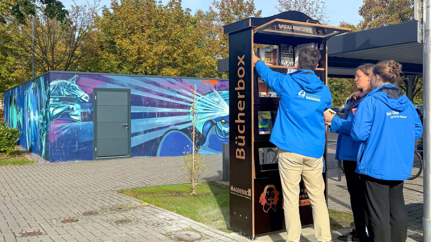 Mitarbeiter von Otto bestücken einen Bücherschrank auf dem Fußweg mit Büchern.