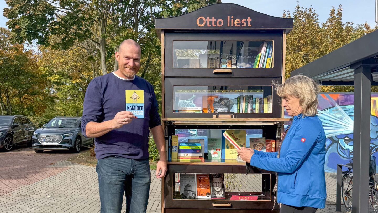 Ein Mann und eine Frau stehen vor einem Bücherschrank auf einem Fußweg.