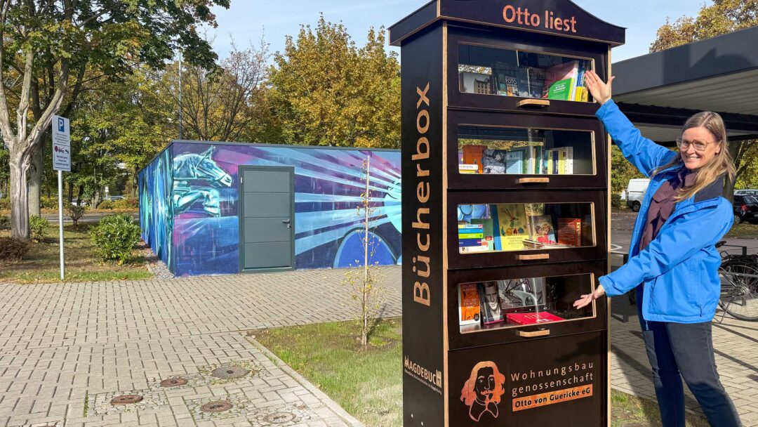 Eine Frau präsentiert einen Bücherschrank auf einem Fußweg.