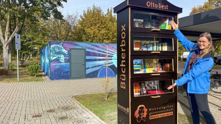 Eine Frau präsentiert einen Bücherschrank auf einem Fußweg.