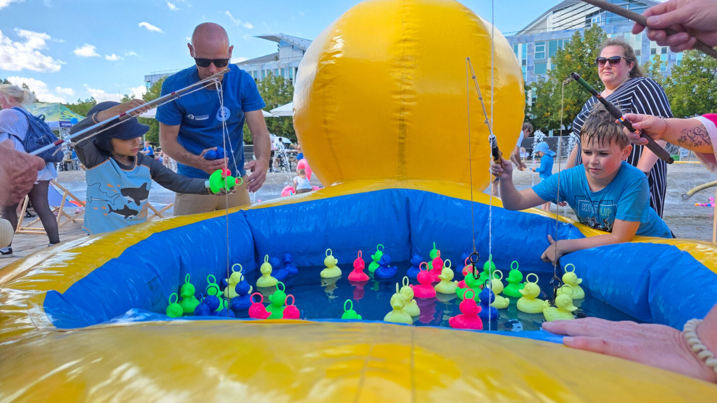 Kinder angel aus einer übergroßen gleb-blauen Plastik-Ente gefüllt mit Wasser kleine Plastikenten.