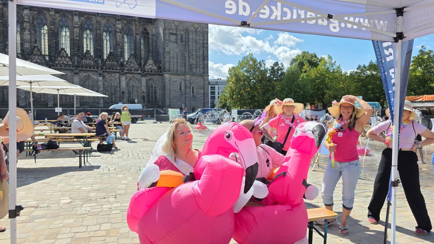 Eine Frau und ein Mann in rosa Flamingo-Kostümen. Dahinter mehrer Menshcen in pinken Shirts und Strohhüten.