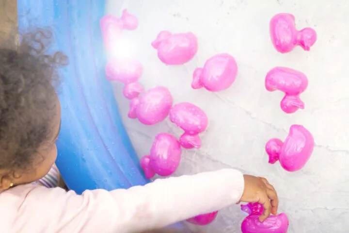 Kinder spielen mit pinken Plastikenten in einem aufblasbaren Pool.