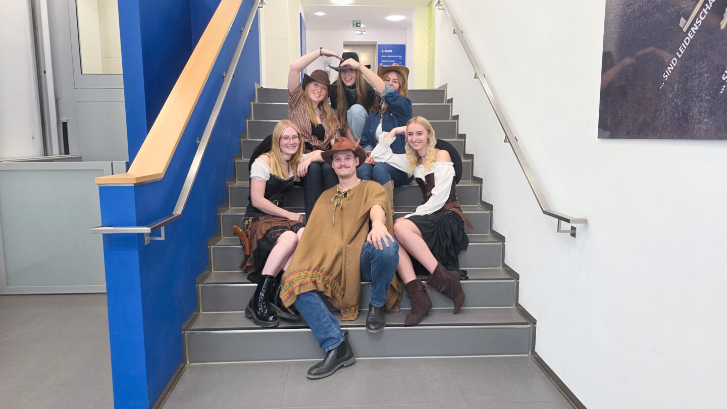 5 Frauen und ein Mann in Westernkleidung sitzen auf einer Treppe und lächeln.